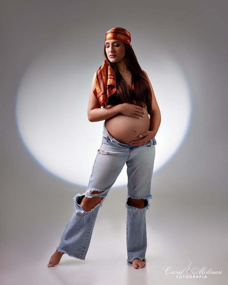 Gestante de turbante e jeans em estúdio, com luz circular ao fundo