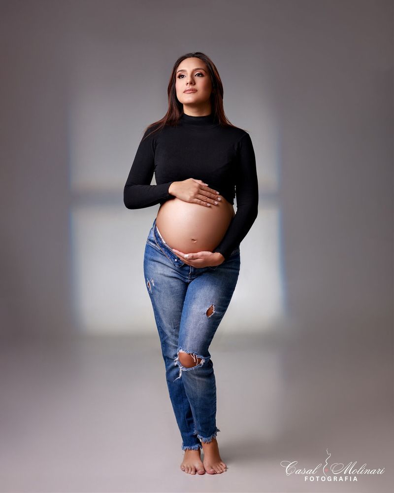 Gestante de blusa preta e jeans rasgado em estúdio