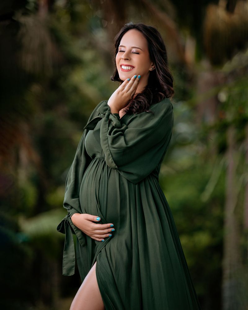 Gestante de vestido verde em jardim, sorrindo